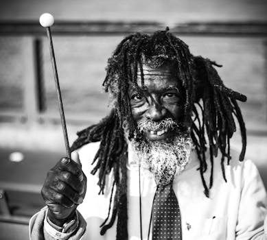Expressive black and white portrait of a man holding a mallet with dreadlocks and a friendly smile.