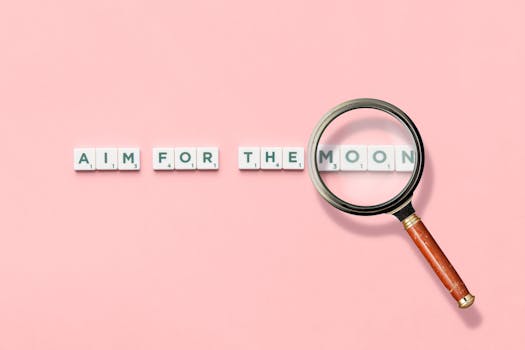 Inspirational quote 'Aim for the Moon' composed with letter tiles and magnifying glass on pink background.